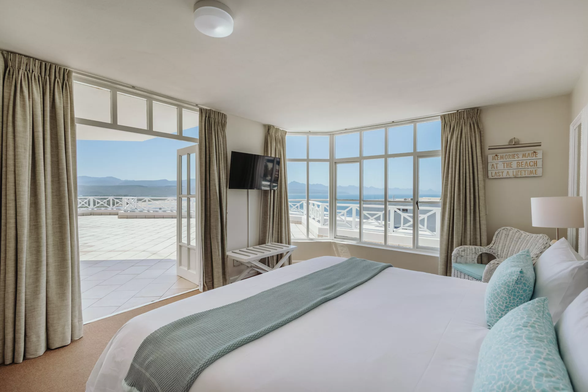 sunny hotel room with king-sized bed, tv, huge balcony, and large window offering sea views of plettenberg bay