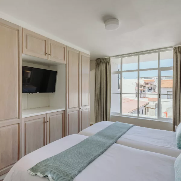sunny hotel room with twin beds, and built in cupboards with a TV