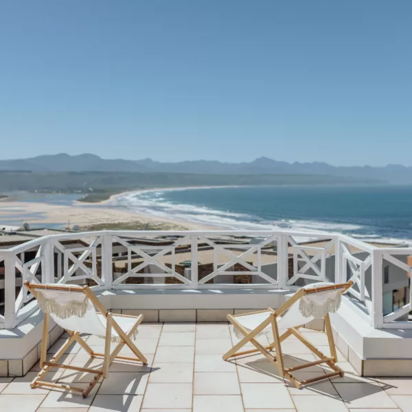 two deck chairs on a balcony overlooking a sunny plettenberg bay