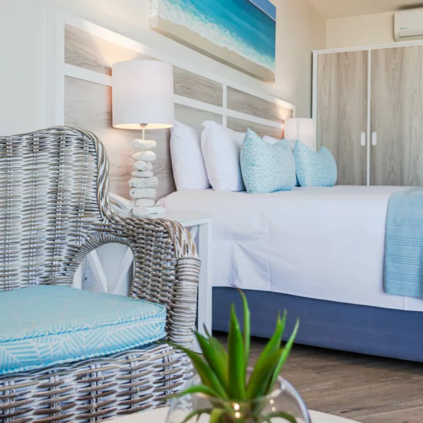 Comfortable bed with sea colour pillows and throw, bedside table and bar fridge in a classic hotel room