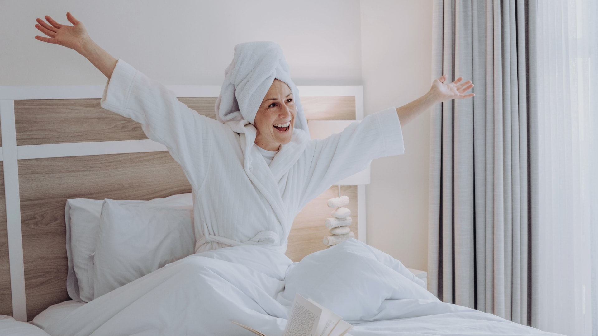 happy woman with arms wide open on a bed dressing in gown