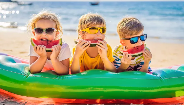 Children eat watermelon on the beach in sunglasses.