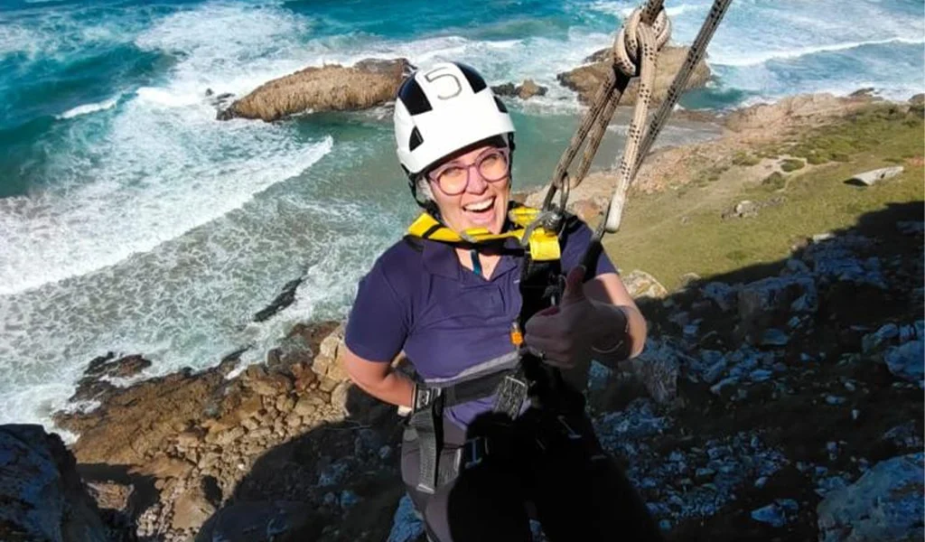 laughing woman abseiling down a cliff above the sea